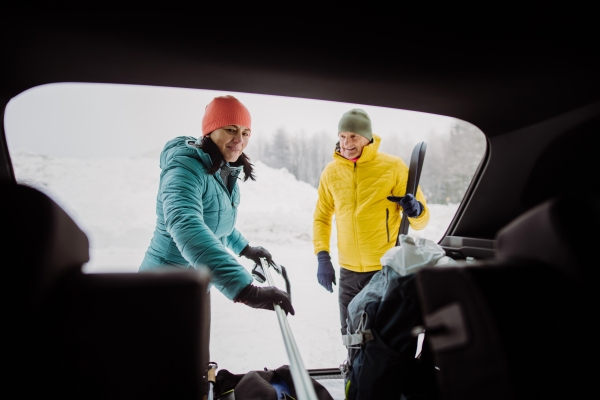 Senior couple near a car trunk preparing for winter skiing.