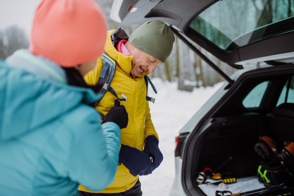 Senior couple near a car trunk preparing for winter skiing.