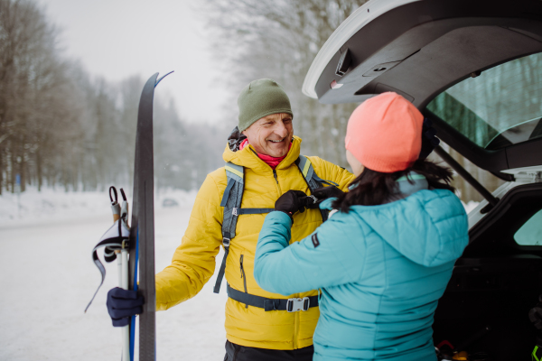 Senior couple near a car trunk preparing for winter skiing.