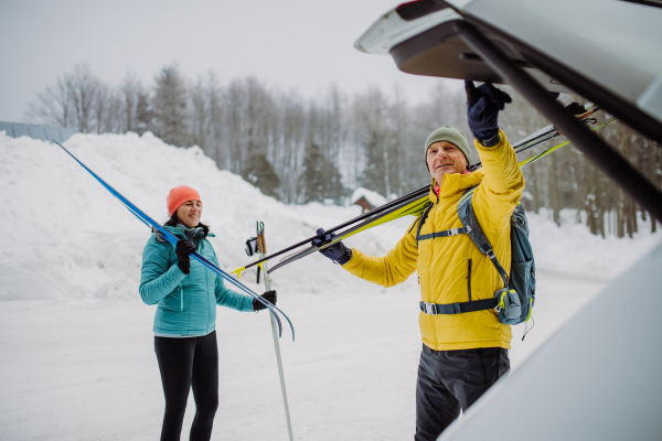 Senior couple near a car trunk preparing for winter skiing.