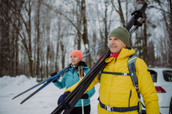 Senior couple crossing winter forest with skis in hands.