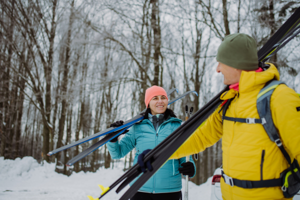 Senior couple crossing winter forest with skis in hands.