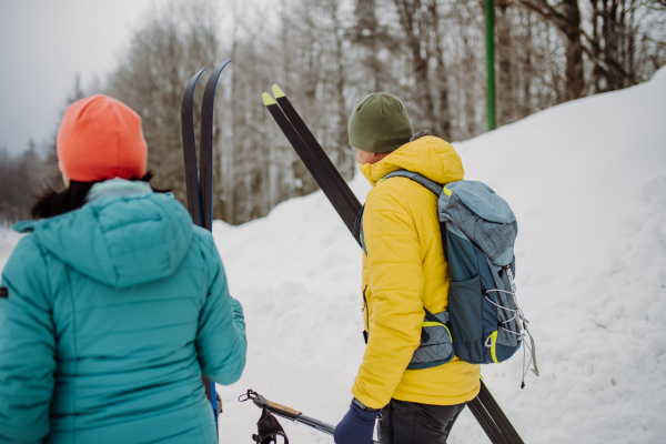 Senior couple crossing winter forest with skis in hands.