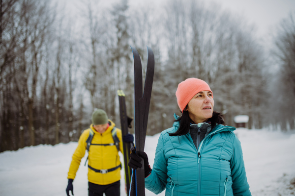 Senior couple crossing winter forest with skis in hands.