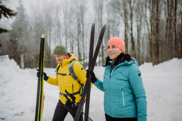 Senior couple crossing winter forest with skis in hands.