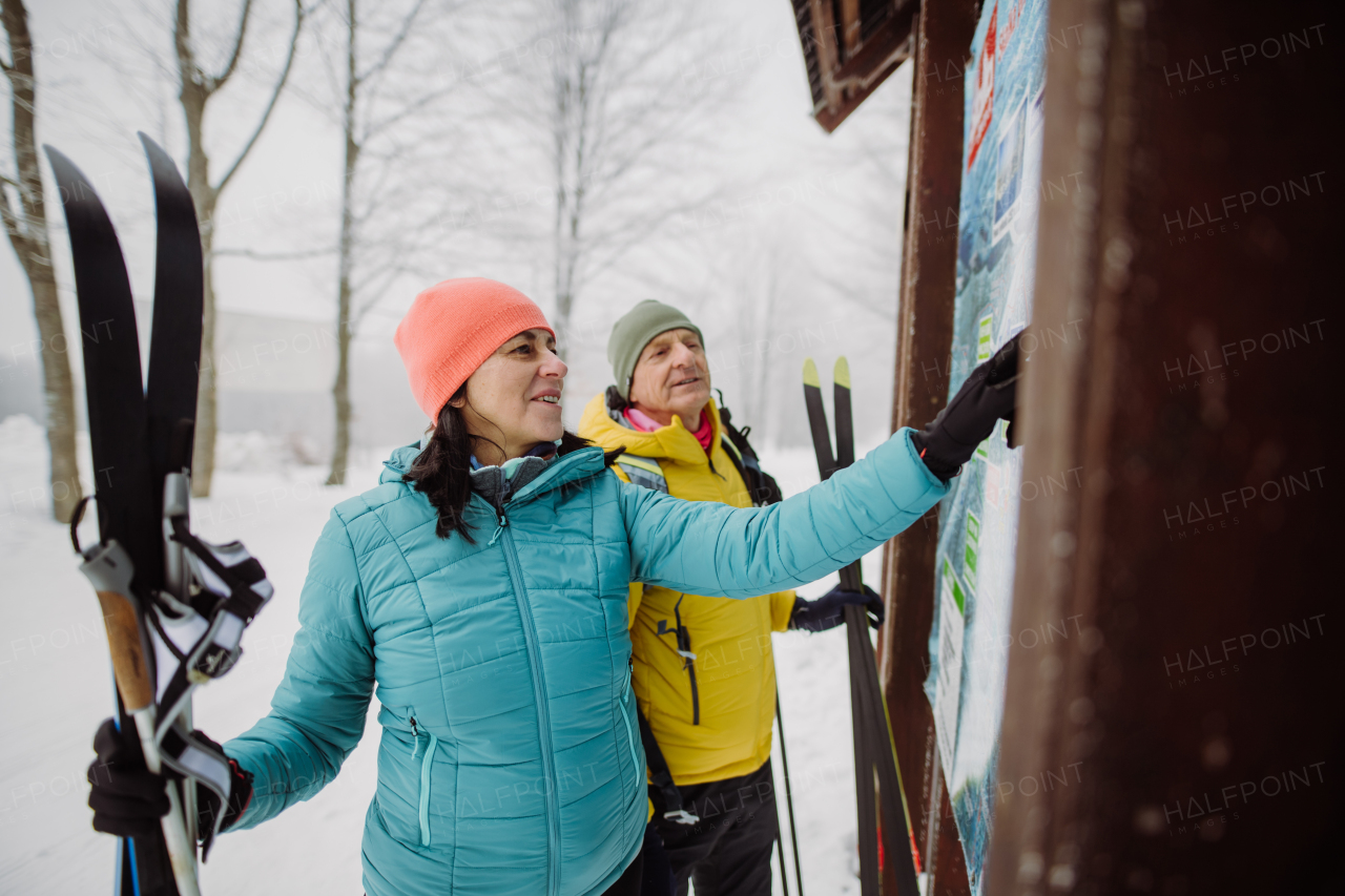 Senior couple looking at a tourist board in the middle of snowy forest.