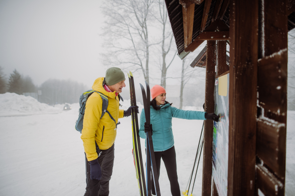 Senior couple looking at a tourist board in the middle of snowy forest.