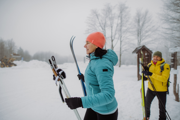 Senior couple crossing winter forest with skis in hands.