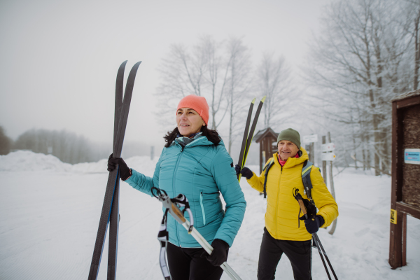 Senior couple crossing winter forest with skis in hands.