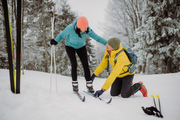 Senior couple putting on skis, preparing for the ride in winter snowy nature.