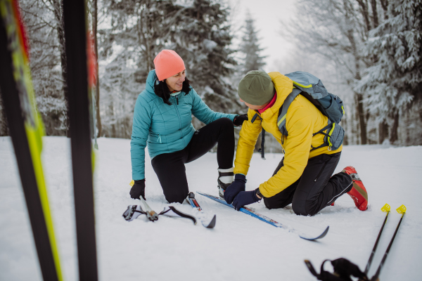 Senior couple putting on skis, preparing for the ride in winter snowy nature.