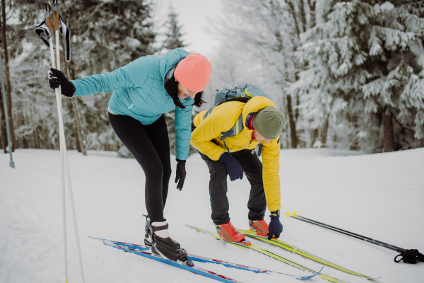 Senior couple putting on skis, preparing for the ride in winter snowy nature.