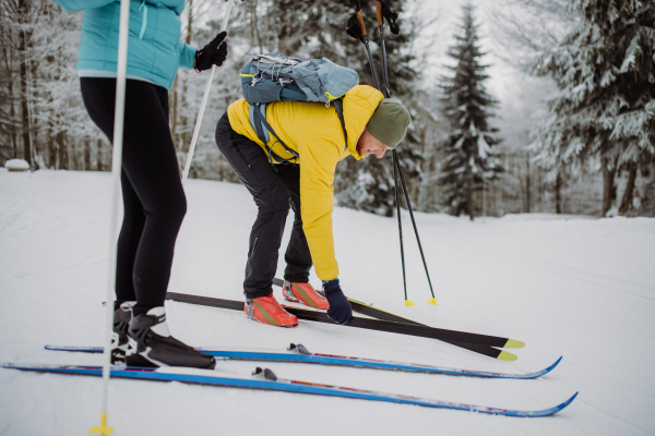 Senior couple putting on skis, preparing for the ride in winter snowy nature.