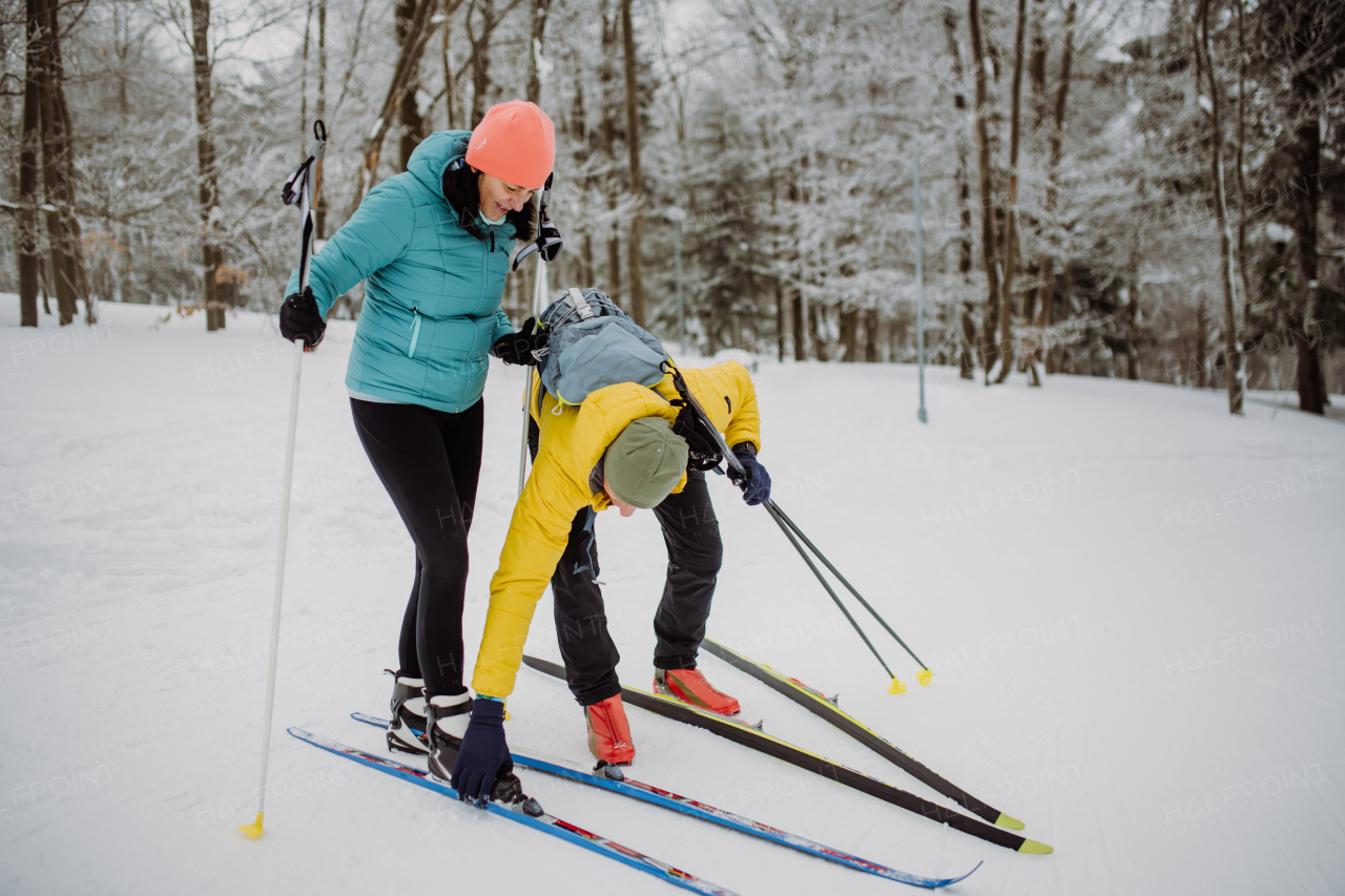 Senior couple putting on skis, preparing for the ride in winter snowy nature.