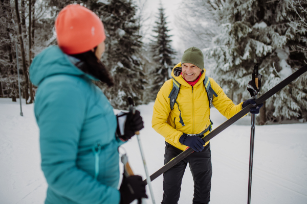 Senior couple crossing winter forest with skis in hands.