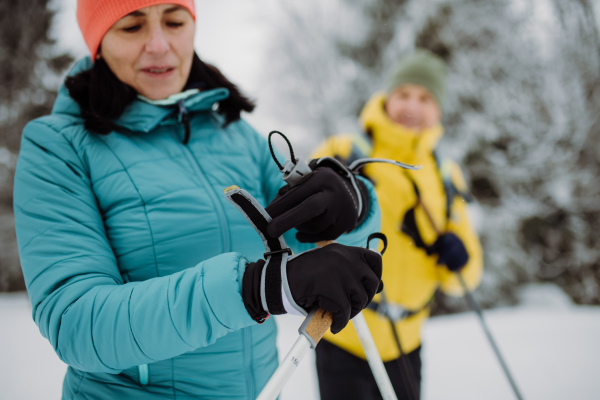 Senior woman putting on a ski gloves, during cross country skiing with her husband