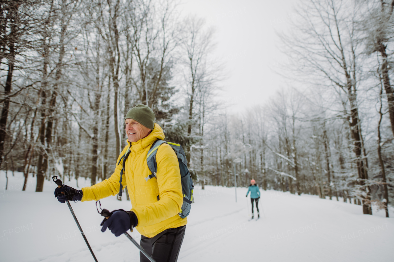 Senior man doing cross country skiing in front of a snowy forest.