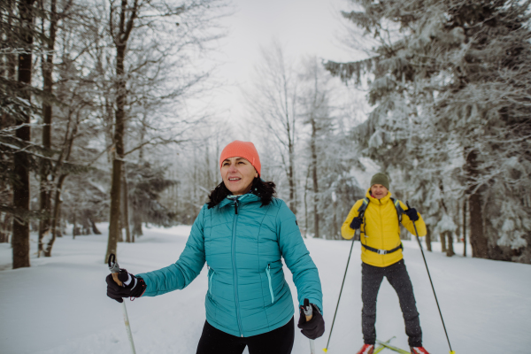 Senior couple skiing together in the middle of snowy forest.