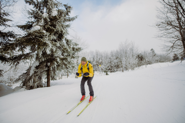 Senior man doing cross country skiing in front of a snowy forest.