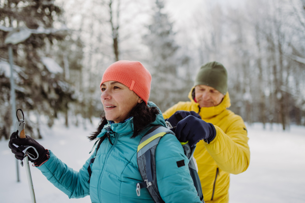 Senior couple skiing together in the middle of snowy forest, having a break.