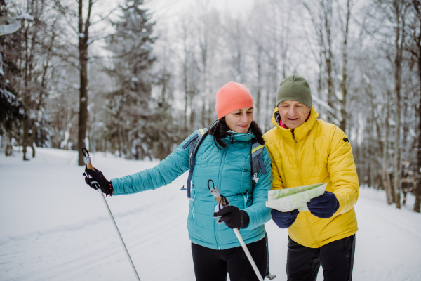 Senior couple looking at paper map during cross country skiing in snowy nature.