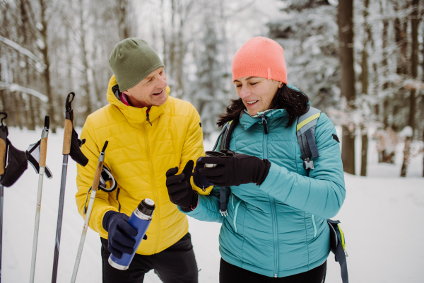 Senior couple resting and drinking hot tea from thermos in the middle of snowy forest.