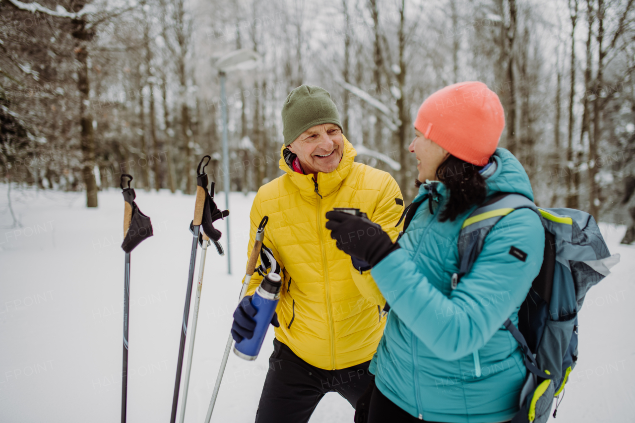 Senior couple resting and drinking hot tea from thermos in the middle of snowy forest.