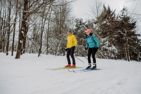 Senior couple skiing together in the middle of snowy forest.