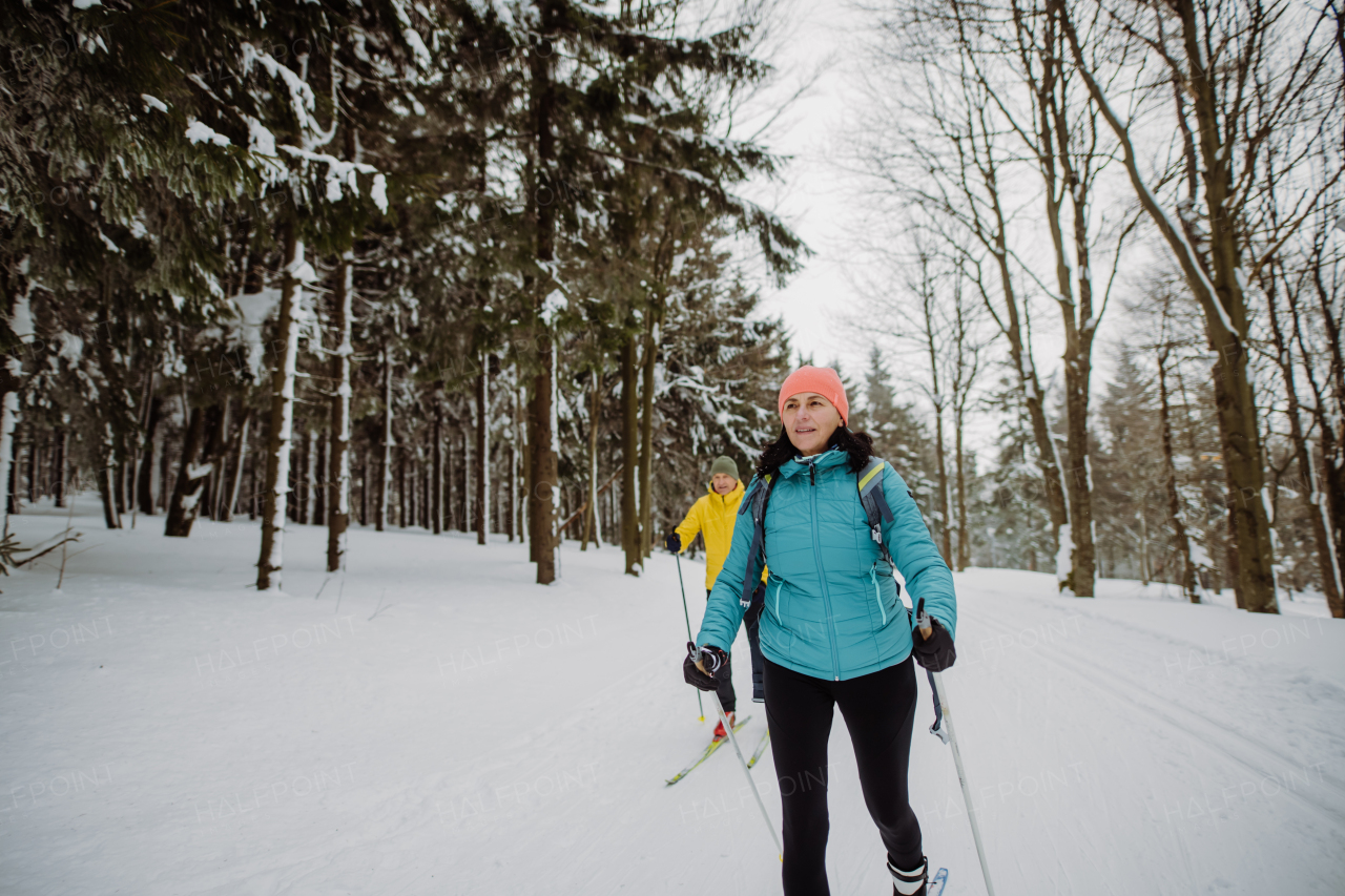 Senior couple skiing together in the middle of snowy forest.