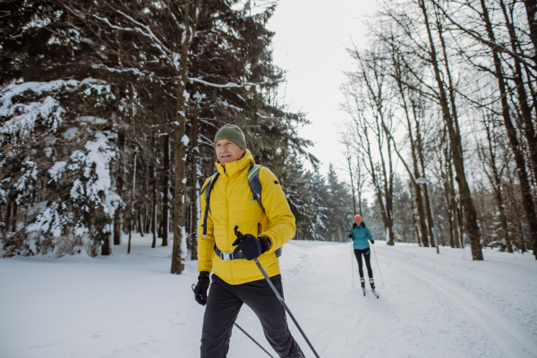 Senior couple skiing together in the middle of snowy forest.