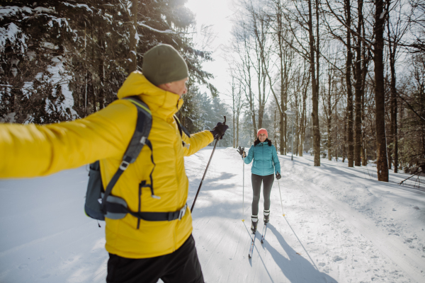 Senior couple skiing together in the middle of snowy forest.