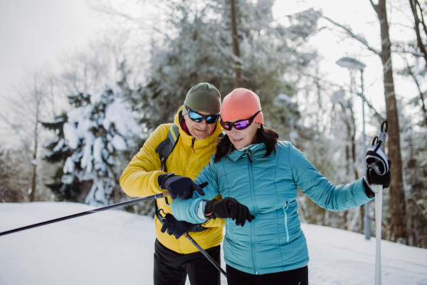 Senior couple looking at a smartwatch during winter skiing.