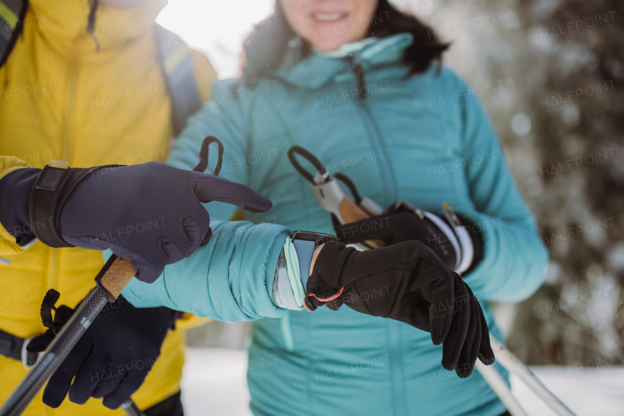 Close up of senior couple looking at a smartwatch during winter skiing.