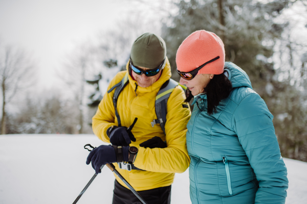 Senior couple looking at a smartwatch during winter skiing.