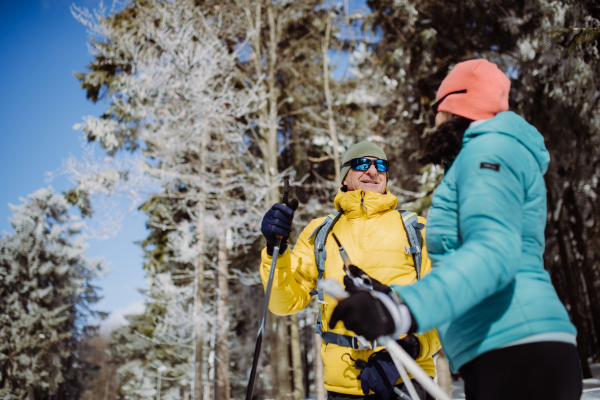 Senior couple skiing together in the middle of snowy forest.