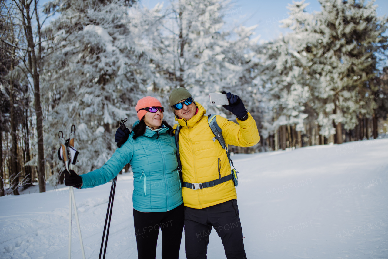 Senior couple taking selfie during cross country skiing in snowy nature.