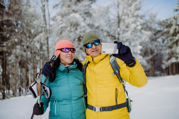 Senior couple taking selfie during cross country skiing in snowy nature.