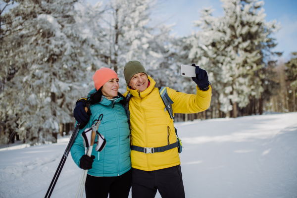 Senior couple taking selfie during cross country skiing in snowy nature.