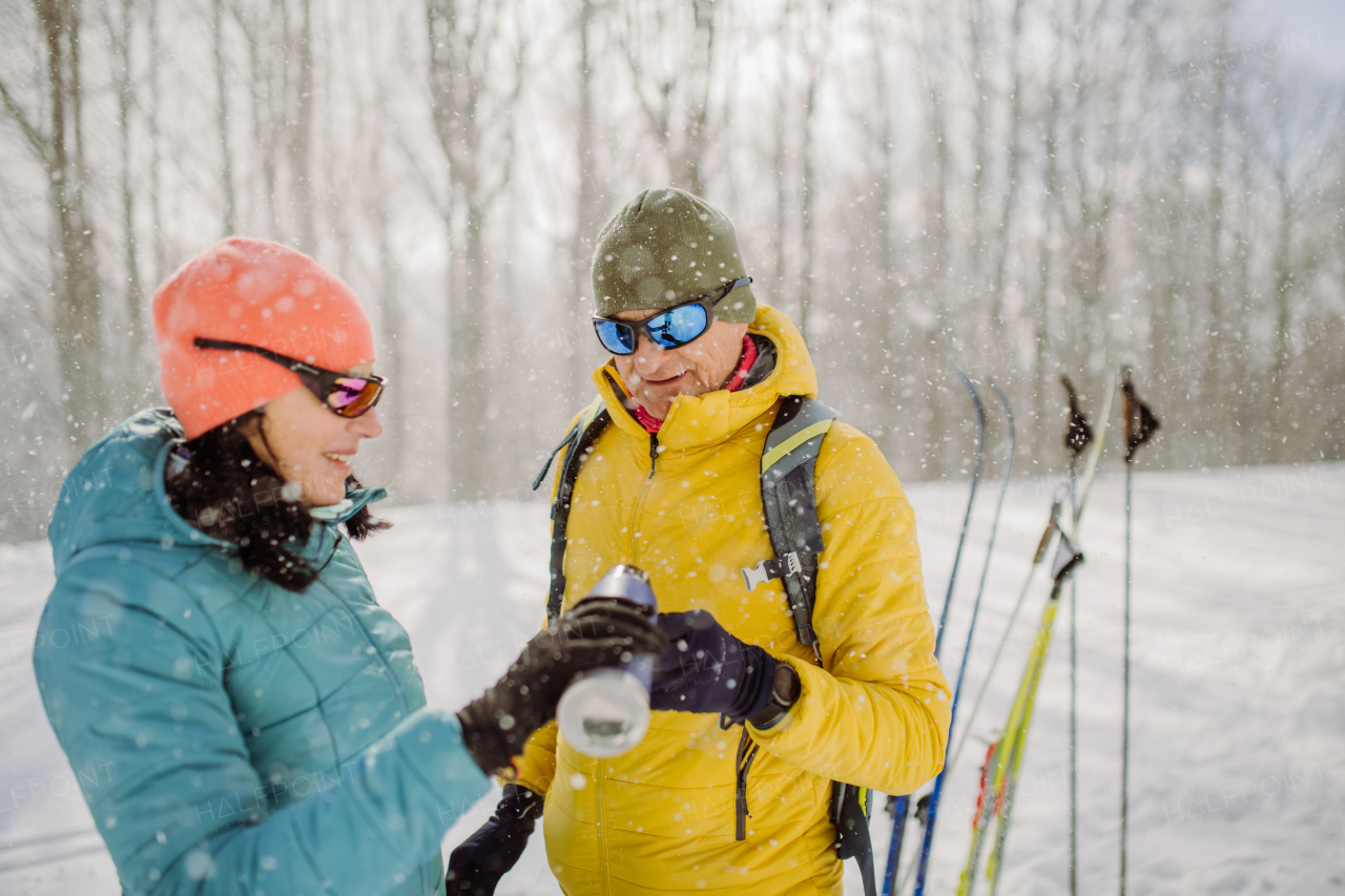 Senior couple resting and drinking hot tea from thermos in the middle of snowy forest.