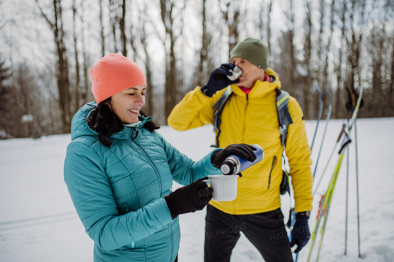 Senior couple resting and drinking hot tea from thermos in the middle of snowy forest.