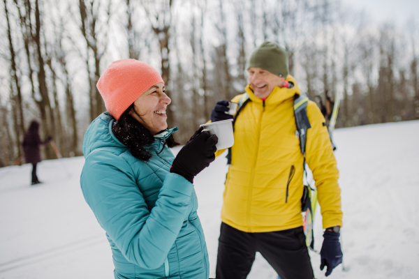 Senior couple resting and drinking hot tea from thermos in the middle of snowy forest.