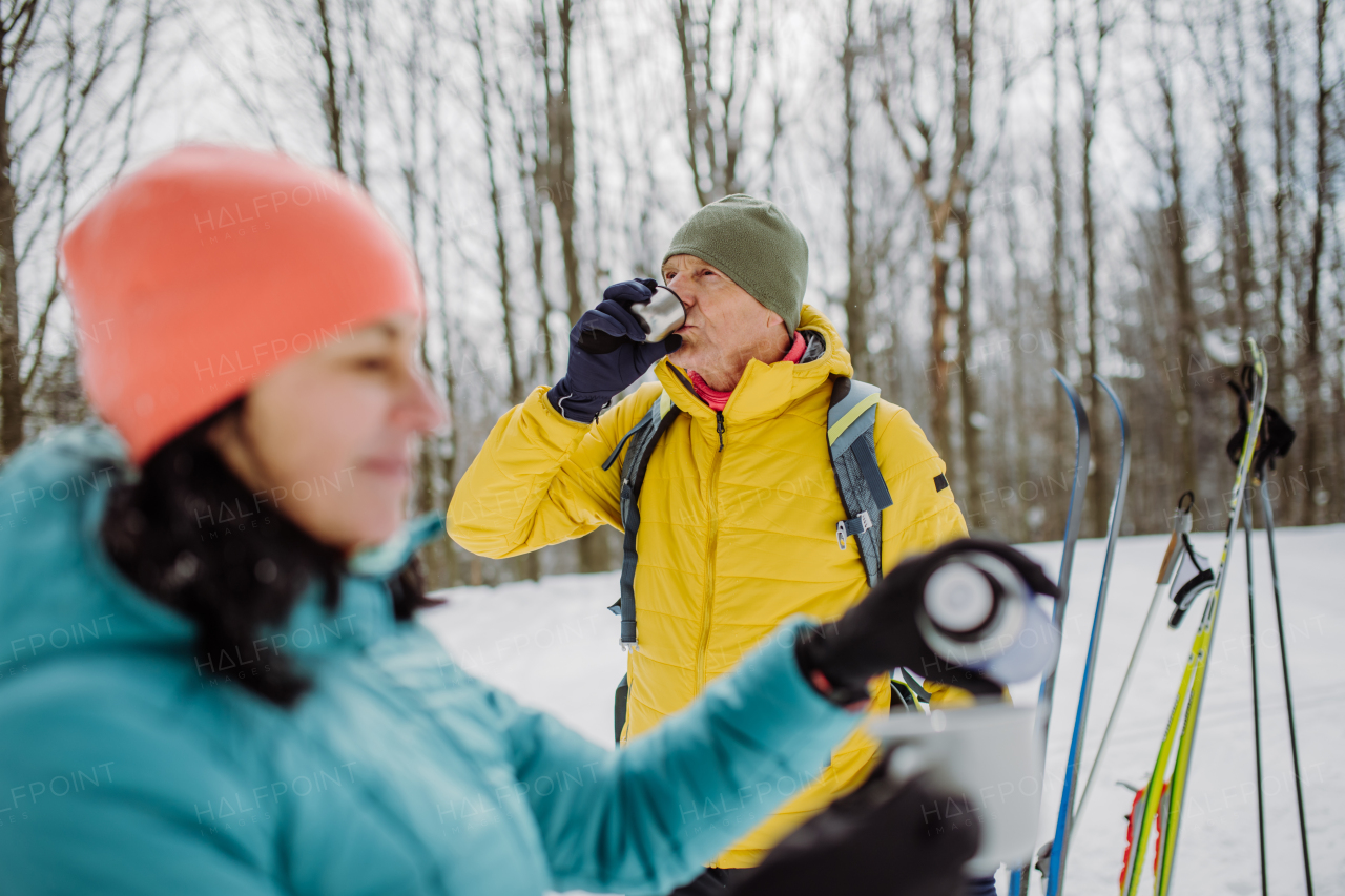 Senior couple resting and drinking hot tea from thermos in the middle of snowy forest.