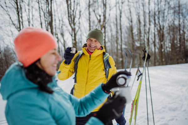 Senior couple resting and drinking hot tea from thermos in the middle of snowy forest.