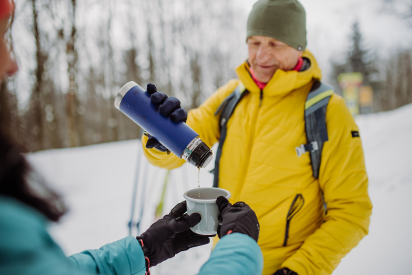 Senior couple resting and drinking hot tea from thermos in the middle of snowy forest.