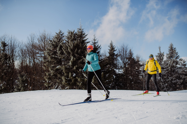 Senior couple skiing together in the middle of snowy forest.