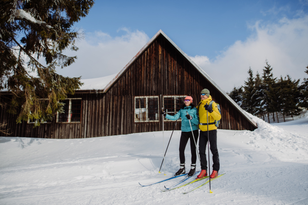 Senior couple having break during skying, next forest snowy cottage.