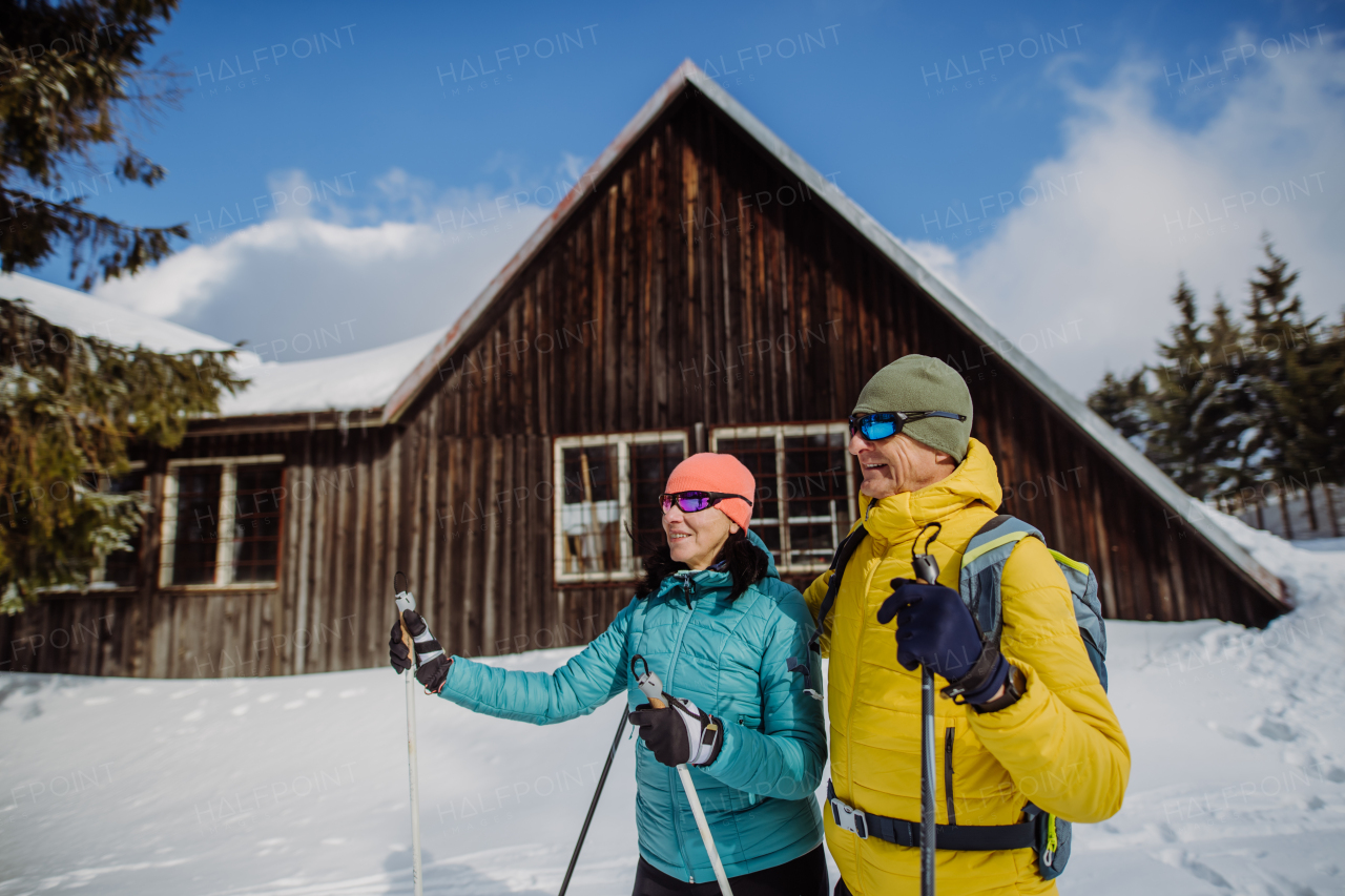 Senior couple having break during skying, next forest snowy cottage.