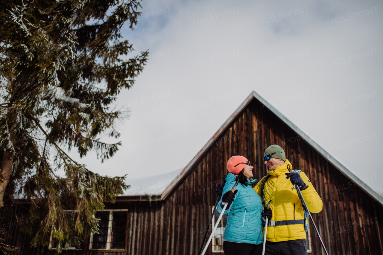 Senior couple having break during skying, next forest snowy cottage.