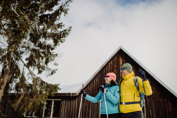 Senior couple having break during skying, next forest snowy cottage.