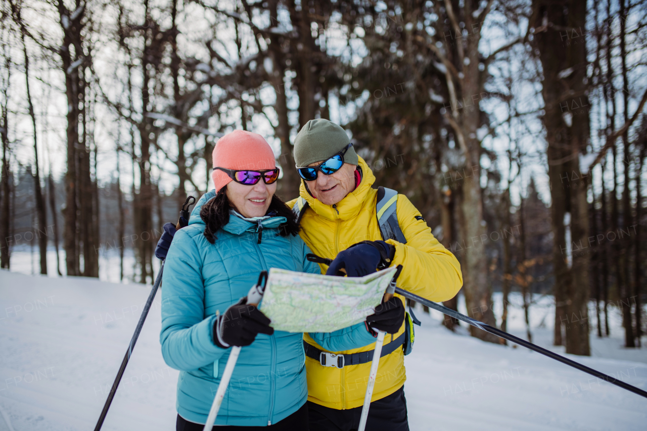 Senior couple looking at paper map during cross country skiing in snowy nature.